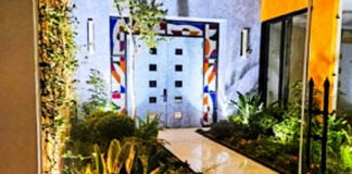 A modern Mexican courtyard with parquet floor and stone double entrance doors to a home. The three sides around the doors feature modernist abstract colors of stained glass.
