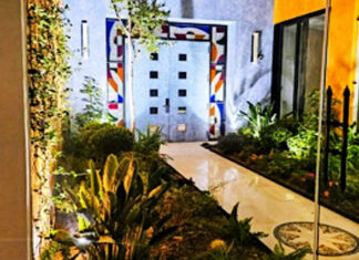 A modern Mexican courtyard with parquet floor and stone double entrance doors to a home. The three sides around the doors feature modernist abstract colors of stained glass.