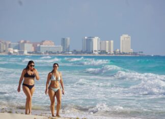 Two women in bikinis walk down the beach in Cancun, Quintana Roo, with the city skyline in the background