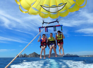 Three people strapped into a yellow parasail connected to a boat off camera. They are in the air slightly above the ocean.