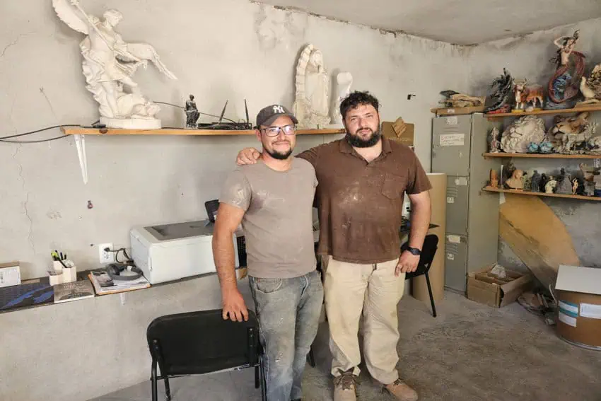 Hugo Uribe (left) and his brother José Uribe (right) standing together in their Canteras Querétaro workshop, with sculptures and materials on shelves.