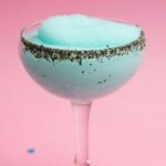 A fluted cocktail glass with a light blue frozen cocktail