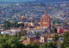 Aerial view of San Miguel de Allende, Mexico, with colonial architecture dominated by tall church steeples and Moorish-style Spanish domed cupolas dotting the skyline.