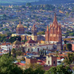 Aerial view of San Miguel de Allende, Mexico, with colonial architecture dominated by tall church steeples and Moorish-style Spanish domed cupolas dotting the skyline.