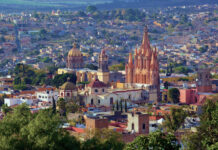 Aerial view of San Miguel de Allende, Mexico, with colonial architecture dominated by tall church steeples and Moorish-style Spanish domed cupolas dotting the skyline.