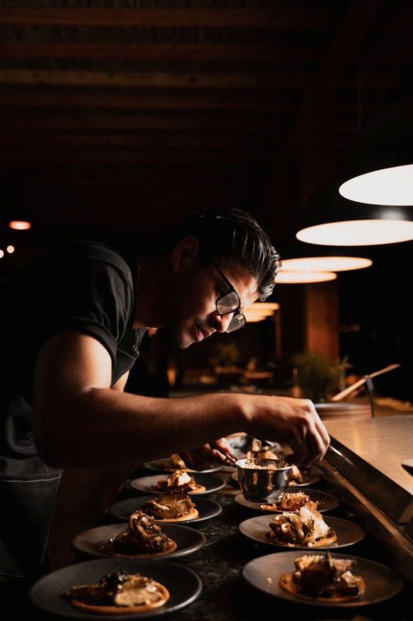 A line chef garnishing small restaurant plates of food in a staging area of the restaurant's kitchen.