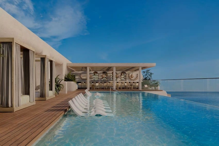 An infinity pool with lounge chairs in Puerto Vallarta leads to an outdoor bar area, overlooking the ocean under a clear blue sky.