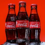 Three bottles of Coca-Cola on a pile of ice cubes and against a red background.