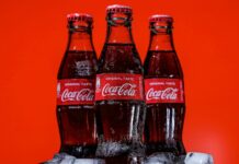 Three bottles of Coca-Cola on a pile of ice cubes and against a red background.