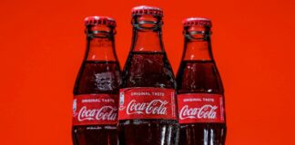 Three bottles of Coca-Cola on a pile of ice cubes and against a red background.