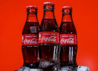 Three bottles of Coca-Cola on a pile of ice cubes and against a red background.