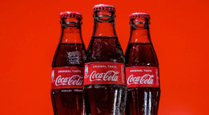 Three bottles of Coca-Cola on a pile of ice cubes and against a red background.