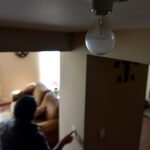 A person touches a light switch during a power outage, while a light bulb remains off in the foreground