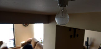 A person touches a light switch during a power outage, while a light bulb remains off in the foreground