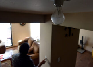 A person touches a light switch during a power outage, while a light bulb remains off in the foreground