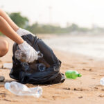 A woman picks up plastic bottles on a beach