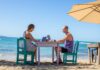 Man and woman work on laptops at a table on a beach