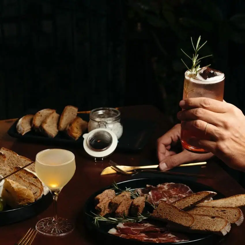 Hand holding cocktail hovers over table of food