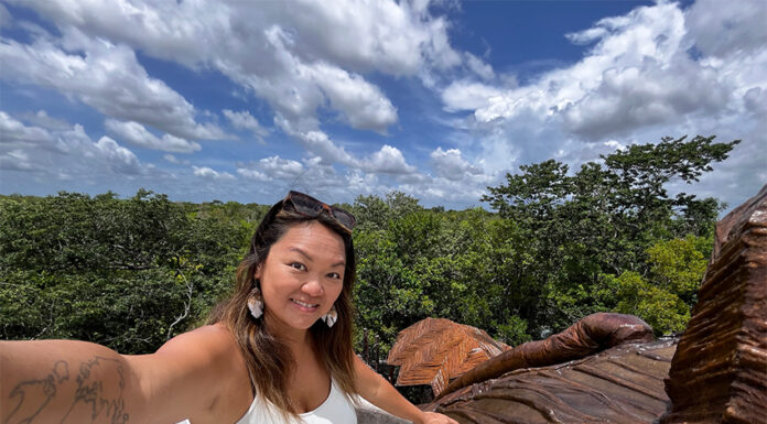 Nellie Huang, a woman with a tattoo of the world map on her arm takes a selfie in a Yucatán Peninsula forest.