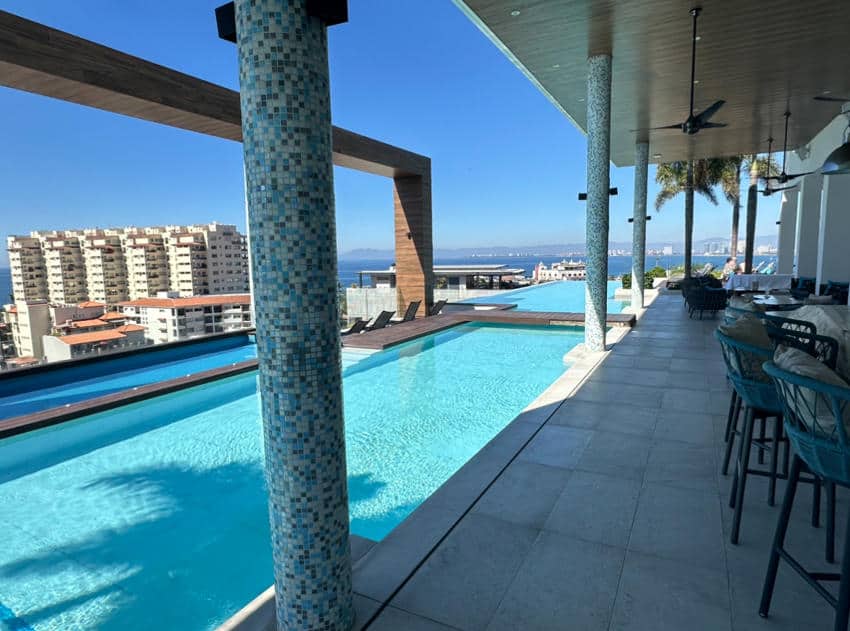 A rooftop bar with a pool that overlooks the ocean and buildings along Puerto Vallarta's coastline.