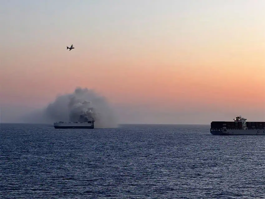 Clouds of smoke roll off a cargo ship at sunset