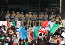 Protesters with Mexican flags and signs stand in front of a wall of California National Guard troops