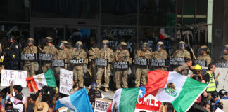Protesters with Mexican flags and signs stand in front of a wall of California National Guard troops