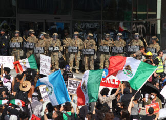Protesters with Mexican flags and signs stand in front of a wall of California National Guard troops