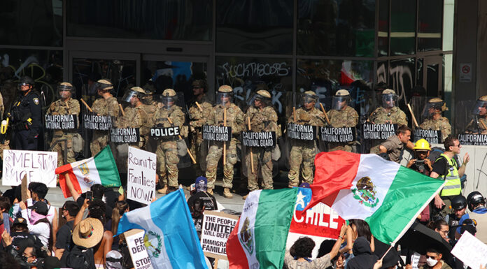 Protesters with Mexican flags and signs stand in front of a wall of California National Guard troops