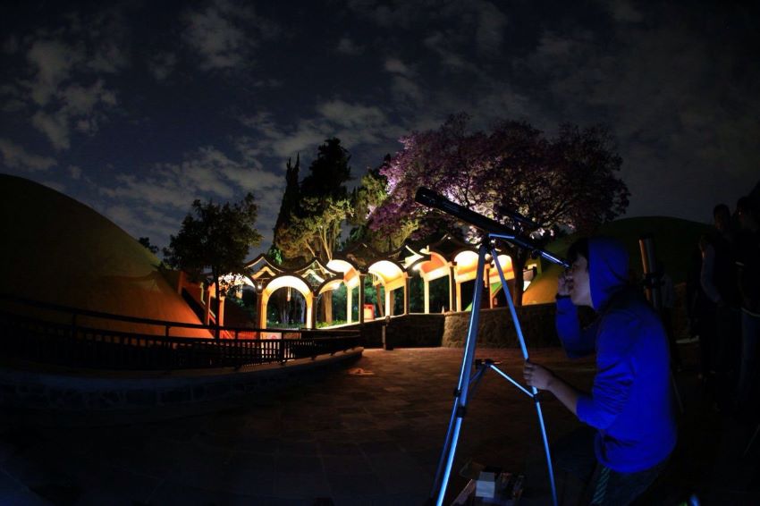person stargazes through telescope in park at night