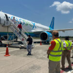 Men deboard a Global X airplane as Mexican airport workers and immigration agents stand by