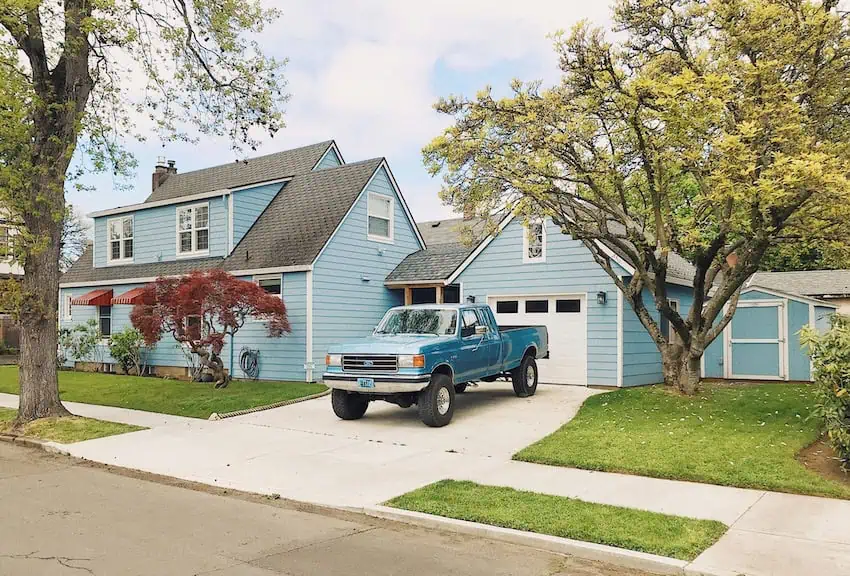 A pickup truck in front of a blue painted house in a stereotypical US suburb