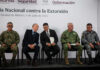 Security chief Omar García Harfuch, Attorney General Gertz and other Mexian officials sit on a stage in front of a banner reading "National Strategy against Extortion" in spanish