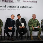 Security chief Omar García Harfuch, Attorney General Gertz and other Mexian officials sit on a stage in front of a banner reading "National Strategy against Extortion" in spanish