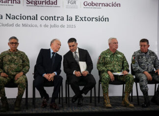Security chief Omar García Harfuch, Attorney General Gertz and other Mexian officials sit on a stage in front of a banner reading "National Strategy against Extortion" in spanish