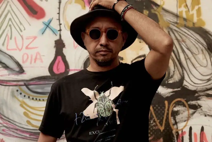 Amador Montes wearing a black hat and sunglasses standing in front of his work