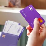 A close up shows a hand with a Nu credit card