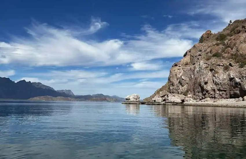 Calm blue waters of the Gulf of California with rocky islands and a rugged coastline under a partly cloudy sky