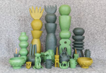 A collection of unique, handcrafted Mexican ceramic art pieces in shades of green and yellow, including tall stacked sculptures, vases, bowls, and whimsical figures, arranged on a textured grey surface.