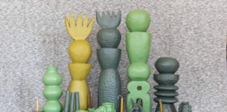 A collection of unique, handcrafted Mexican ceramic art pieces in shades of green and yellow, including tall stacked sculptures, vases, bowls, and whimsical figures, arranged on a textured grey surface.