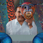 Artist Jacobo Ángeles holding a traditional Oaxacan folk art mask in front of his face.