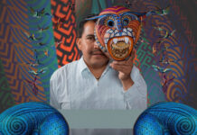 Artist Jacobo Ángeles holding a traditional Oaxacan folk art mask in front of his face.