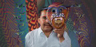 Artist Jacobo Ángeles holding a traditional Oaxacan folk art mask in front of his face.