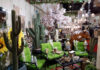 A vibrant Mexican-themed home decor display featuring large artificial cacti, bright green patio furniture, sunflowers, a cow statue, and various rustic lanterns and lighting fixtures, suggesting an eclectic outdoor living space.