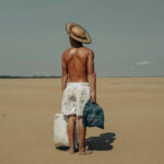 A photo of a shirtless man wearing white shorts stood on a beach