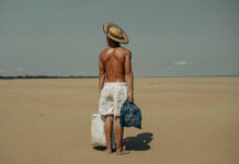 A photo of a shirtless man wearing white shorts stood on a beach