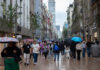 people walk through mexico city with umbrellas, with the latin america tower in the backgound