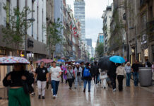people walk through mexico city with umbrellas, with the latin america tower in the backgound