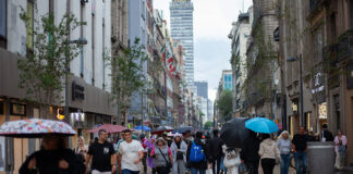 people walk through mexico city with umbrellas, with the latin america tower in the backgound