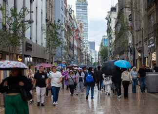 people walk through mexico city with umbrellas, with the latin america tower in the backgound